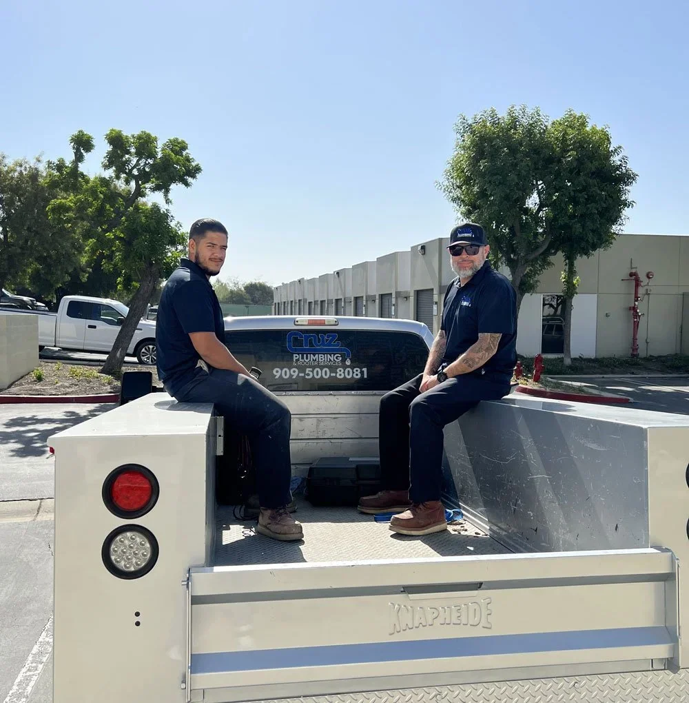 Two Cruz Plumbing technicians with a water heater on a service truck